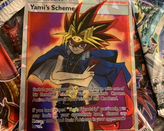 Op de afbeelding: Een holografische Pokemon-verzamelkaart met Yami, een personage uit de anime-serie Yu-Gi-Oh! De kaart heeft de titel "Yami's Scheme" en is een Supporter-kaart. De kaarttekst beschrijft het effect van de kaart, waardoor de speler het Actieve Pokemon van zijn tegenstander kan ruilen met een van zijn Bank-Pokemon. De kaart is genummerd 001/002.