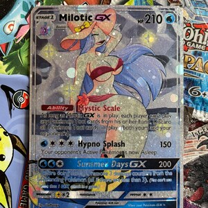 May include: A holographic Pokemon trading card featuring Milotic GX, a water-type Pokemon with a blue and pink color scheme. The card has a silver background with glitter and features the text "Mystic Scale" and "Hypno Splash".