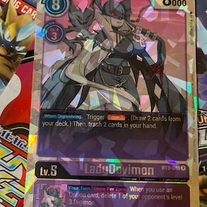 Può includere: Una carta da gioco di scambio di colore viola e argento con un personaggio femminile di anime con lunghi capelli bianchi e un abito nero e rosso. La carta è intitolata "Lady Devimon" e ha un livello di 5. La carta è del gioco di carte collezionabili Digimon.