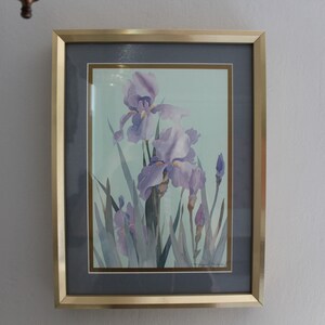May include: A framed watercolor painting of purple irises with green leaves on a light blue background.