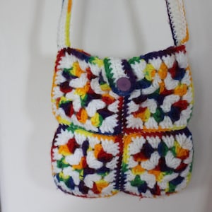 May include: A rainbow crochet shoulder bag with a purple button closure. The bag is made of white, red, orange, yellow, green, blue, and purple yarn.