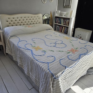 May include: A white tufted headboard with a white and blue floral patterned bedspread. The bedspread has a blue and white ruffled trim.
