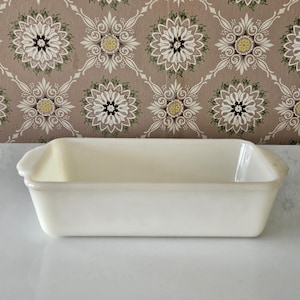 May include: A rectangular, off-white baking dish with rounded corners and small handles. The dish is set against a patterned background of brown and white floral designs, creating a vintage aesthetic.