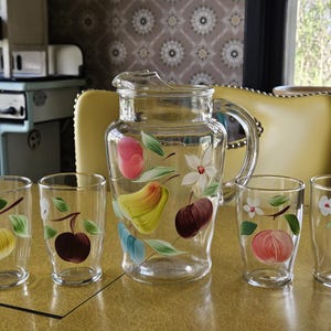 May include: A set of six vintage glass tumblers and a pitcher with hand-painted fruit designs. The pitcher has a pear, apple, and cherry design. The tumblers have a variety of fruit designs, including pears, apples, and cherries.