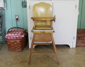 May include: A vintage wooden high chair with a yellow padded seat and a white trim. The chair has a tray and a footrest. The chair is in good condition and would be a great addition to any home.