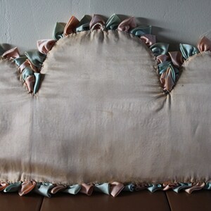 May include: A cream-colored pillow with a ruffled edge. The ruffles are made of pink and green fabric.