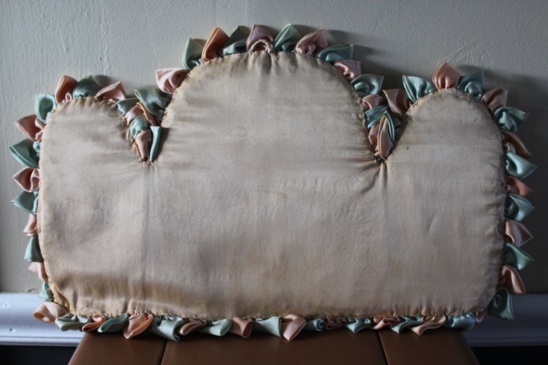 May include: A cream-colored pillow with a ruffled edge. The ruffles are made of pink and green fabric.