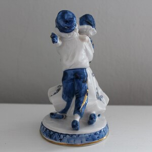 May include: A porcelain figurine of a couple dancing, painted in blue and white with gold accents. The man is wearing a blue hat and the woman is wearing a white dress with blue trim.
