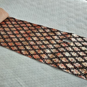 May include: A rolled-up yoga mat with a patterned design. The mat features a black lattice pattern over a floral design in shades of peach, cream, and red. The rolled end is a solid peach color.