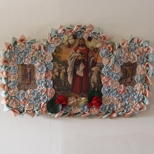 May include: A framed religious image of Jesus carrying a lamb, surrounded by a decorative border of fabric flowers in shades of pink, blue, and green.