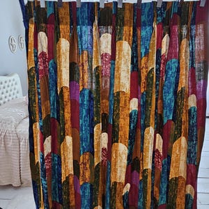 May include: A colorful curtain with a repeating pattern of vertical shapes in shades of brown, orange, blue, red, and white. The curtain is hanging in front of a white wall and a bed with a white headboard.