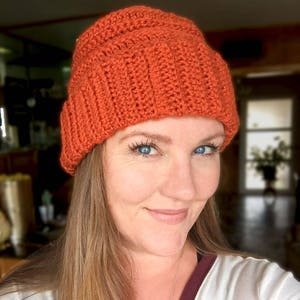 May include: A woman wearing a bright orange crocheted beanie hat. The hat has a ribbed texture and a slouchy fit.