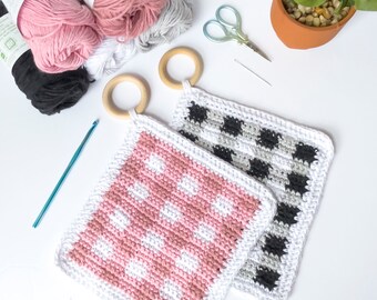 May include: Two crocheted pot holders with wooden handles. One pot holder is pink and white with a polka dot pattern. The other pot holder is black and white with a checkered pattern.