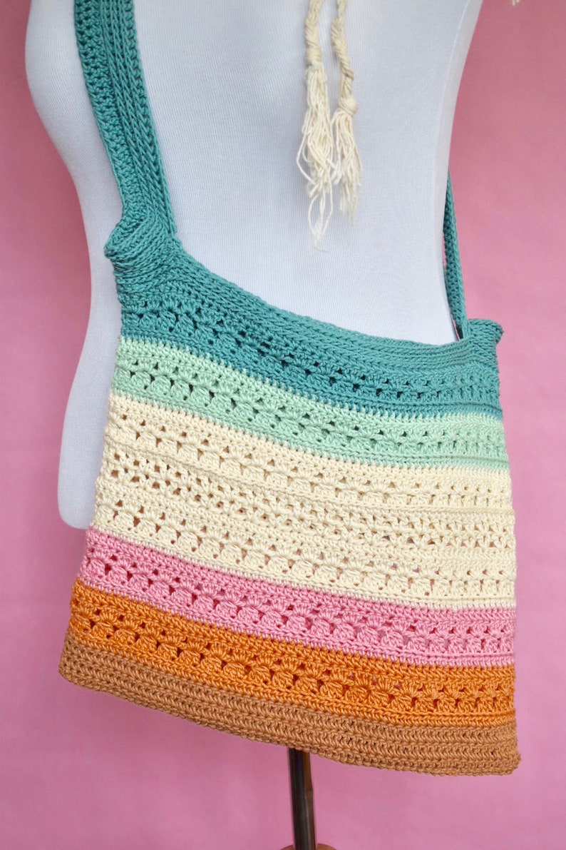 May include: A multi-colored crocheted tote bag with a long strap. The bag is made with a variety of stitches and has a striped pattern in shades of teal, green, cream, pink, and brown.