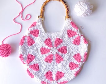 May include: A white crocheted handbag with pink flower designs and a wooden handle.