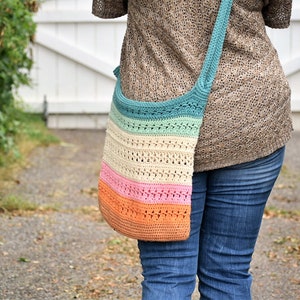 May include: A multi-colored crocheted tote bag with a long strap worn over the shoulder. The bag is made with a variety of colors, including teal, cream, pink, and orange.