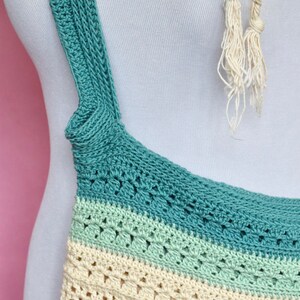 May include: A crocheted tote bag with a multi-colored striped design. The bag has a teal, light green, cream, and pink color scheme. The bag has a long strap that is crocheted in teal.