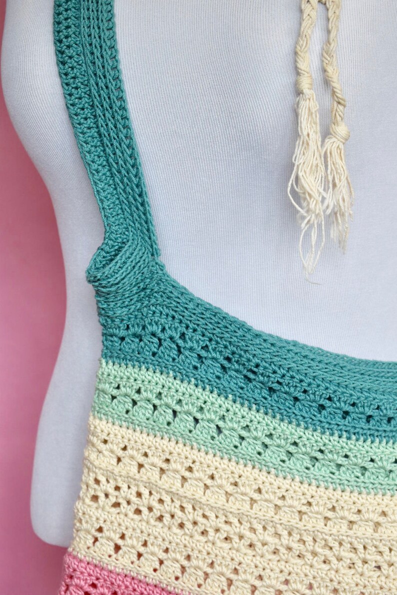 May include: A crocheted tote bag with a multi-colored striped design. The bag has a teal, light green, cream, and pink color scheme. The bag has a long strap that is crocheted in teal.