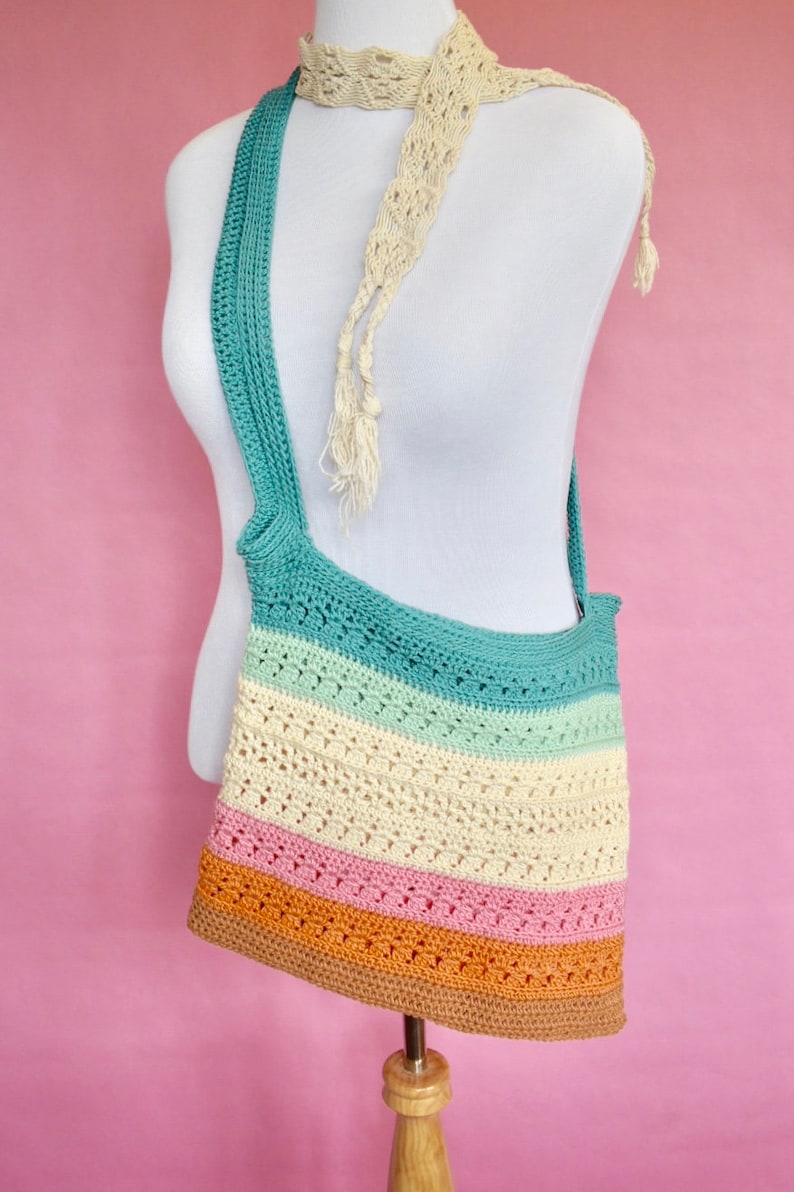 May include: A multi-colored crocheted tote bag with a long strap. The bag is made with a variety of colors, including teal, light green, cream, pink, and orange. The bag is displayed on a white mannequin.