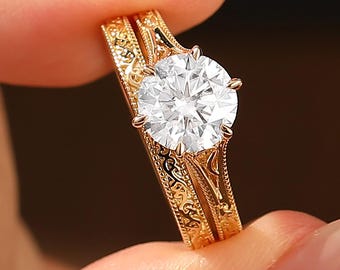 May include: A gold engagement ring set with a large, round-cut diamond. The band has an intricate, engraved pattern. The ring is held against a dark background, highlighting its sparkle and detail. A matching band is also visible.