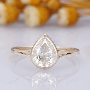 Pu&ograve; includere: Un anello di fidanzamento con un diamante a forma di pera incastonato in una fascia d'oro. L'anello ha un design semplice con un solo diamante al centro.