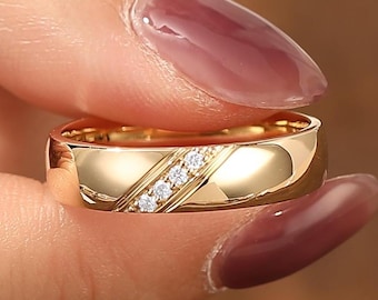 May include: A polished gold band ring featuring a diagonal channel set with four small, clear, round-cut stones. The metal surface is smooth and reflective, showcasing a clean, minimalist design with a single slanted accent across the center.