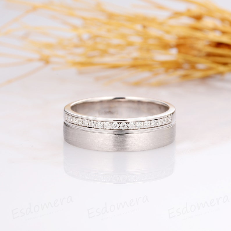 May include: A silver wedding band with a row of small diamonds set in a channel setting. The band has a brushed finish.