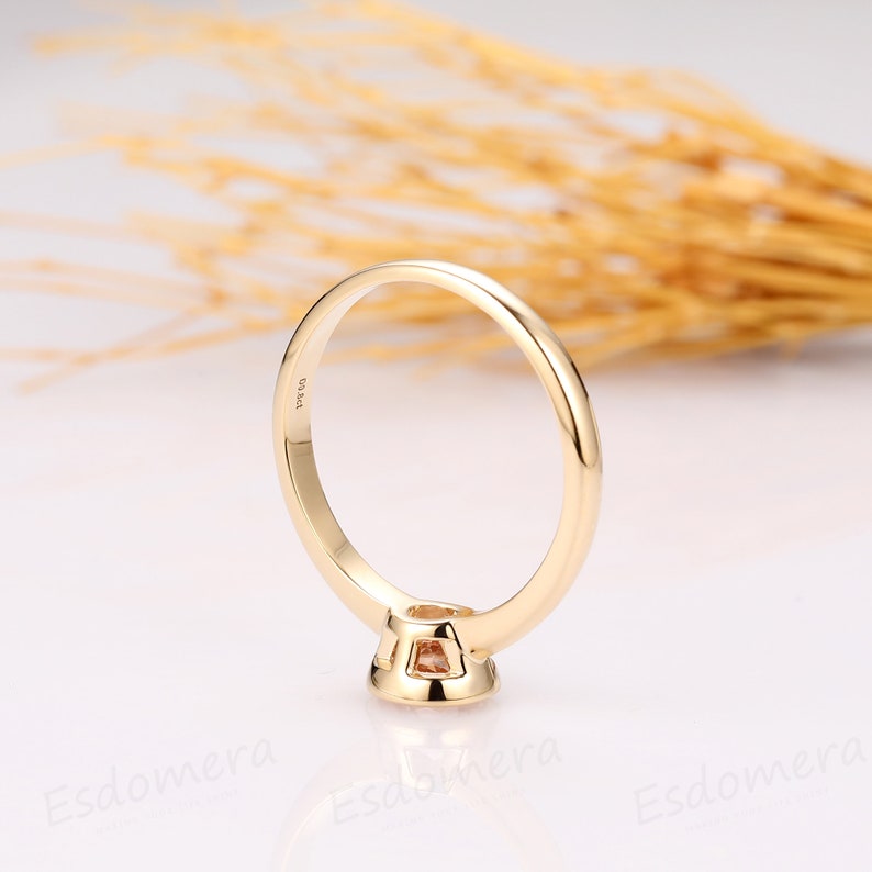 A gold ring with a small, round, light brown gemstone set in the center. The ring is simple and elegant, with a smooth band.