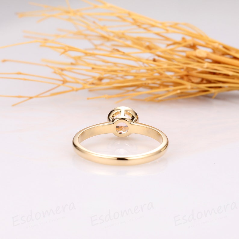 A gold solitaire engagement ring with a round, clear gemstone set in a simple, delicate band.