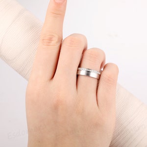 May include: A silver wedding band with a row of small diamonds set in the band.