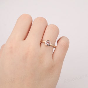 A delicate gold ring with a bezel setting featuring a round, light pink gemstone.