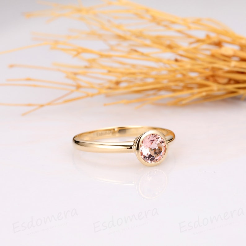 A delicate gold ring with a round, bezel-set pink gemstone. The ring is simple and elegant, perfect for a minimalist style.