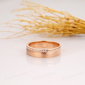 May include: A rose gold wedding band with a row of small diamonds set into the band.