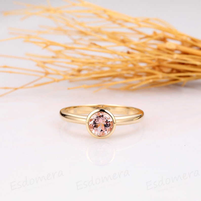 A delicate gold ring with a bezel setting featuring a round, pale pink gemstone.