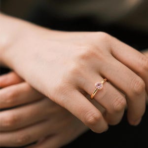 A delicate solid yellow gold ring with a bezel setting featuring a round, light pink gemstone.