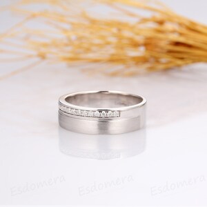 May include: A silver wedding band with a row of small diamonds set into the band.