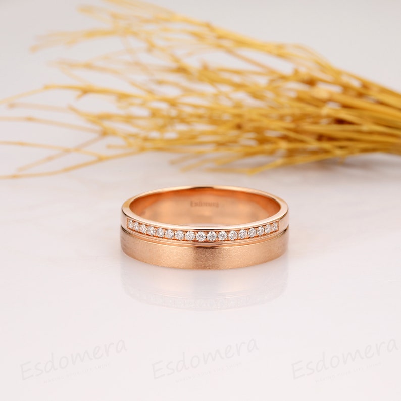 May include: A rose gold wedding band with a row of small diamonds set in a channel setting. The band has a brushed finish.