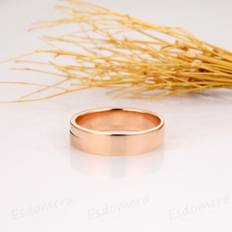 May include: A rose gold wedding band with a flat, polished surface and a subtle groove around the edge.