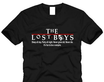 Puede incluir: Camiseta negra con texto blanco que dice "THE LOST BOYS" y la cita "Sleep all day. Party all night. Never grow old. Never die. It's fun to be a vampire."