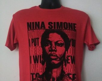 May include: Red t-shirt with a black and white image of Nina Simone. The text on the shirt reads "Nina Simone Don't Let Me Understand You I Put Feel I Wish What To See On New Fans".