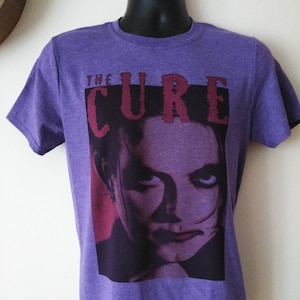 May include: Purple t-shirt with a graphic print of a person's face and the text "THE CURE" in red.
