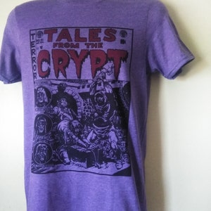 May include: Purple t-shirt featuring a graphic print of a comic book cover with the text "Tales from the Crypt" and a scary illustration.