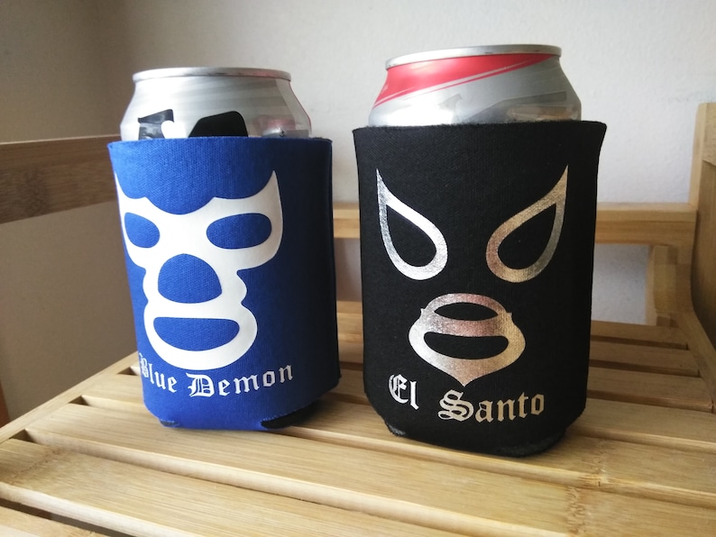Pu&ograve; includere: Due refrigeratori per lattine in neoprene blu e nero con maschere da wrestling bianche e argentate e il testo "Blue Demon" e "El Santo".