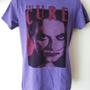 May include: Purple t-shirt with a graphic print of a person's face and the text "THE CURE" in red.