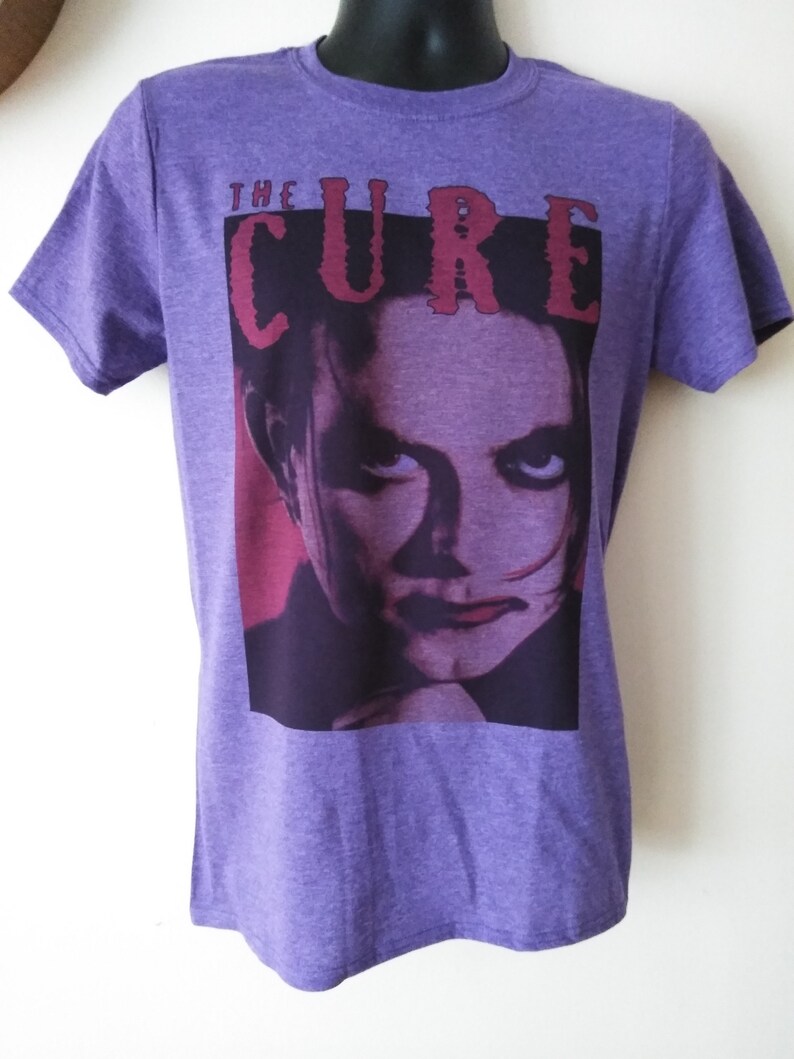 May include: Purple t-shirt with a graphic print of a person's face and the text "THE CURE" in red.