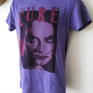 May include: Purple t-shirt with a graphic print of a woman's face and the text "THE CURE" in red.