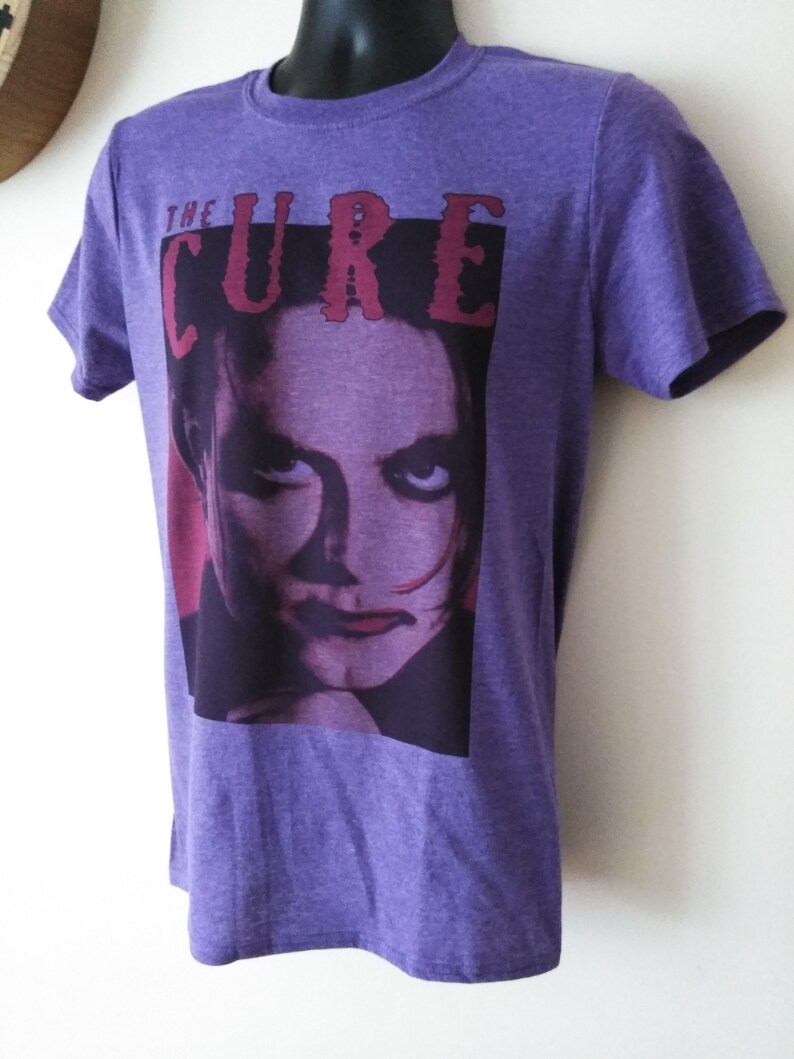 May include: Purple t-shirt with a graphic print of a woman's face and the text "THE CURE" in red.