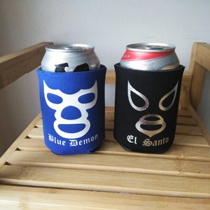 Pu&ograve; includere: Due refrigeratori per lattine in neoprene blu e nero con disegni di maschera da wrestling. Il refrigeratore blu ha una maschera bianca con il testo "Blue Demon" e il refrigeratore nero ha una maschera argentata con il testo "El Santo".