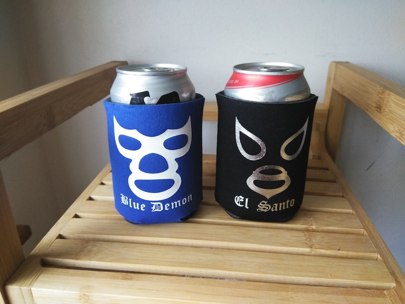 Pu&ograve; includere: Due refrigeratori per lattine in neoprene blu e nero con disegni di maschera da wrestling. Il refrigeratore blu ha una maschera bianca con il testo "Blue Demon" e il refrigeratore nero ha una maschera argentata con il testo "El Santo".