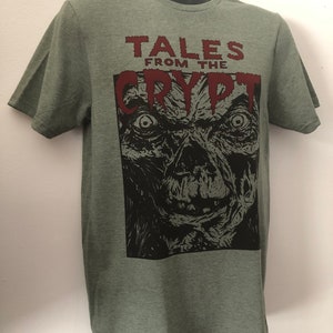May include: Green t-shirt with a black and white illustration of a monster's face and the text "Tales from the Crypt" in red.